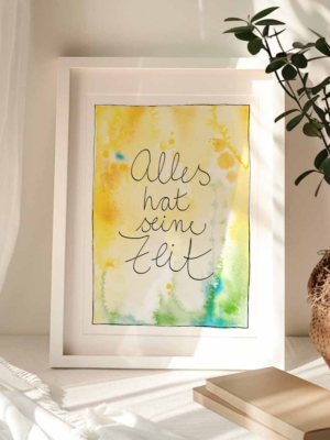 Gerahmter Kunstdruck mit Aquarellhintergrund in Goldgelb- und Grüntönen mit blauen Sprenklern. In der Mitte steht der Text „Alles hat seine Zeit".