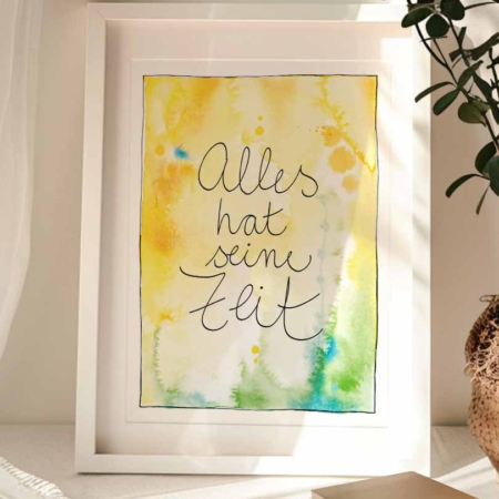 Gerahmter Kunstdruck mit Aquarellhintergrund in Goldgelb- und Grüntönen mit blauen Sprenklern. In der Mitte steht der Text „Alles hat seine Zeit".