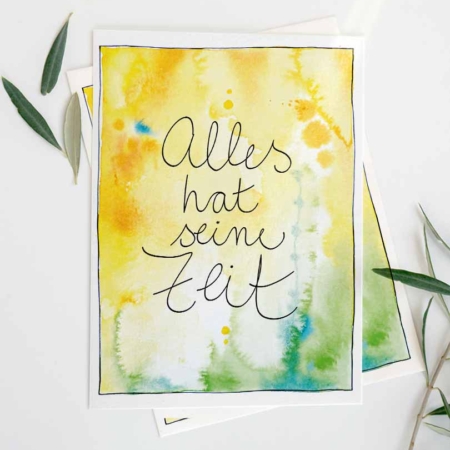 Eine Grußkarte mit Aquarellhintergrund in Goldgelb- und Grüntönen mit blauen Sprenklern. In der Mitte steht der Text „Alles hat seine Zeit".