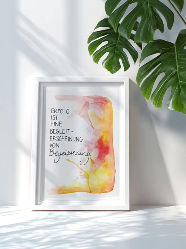 Ein Kunstdruck mit Aquarellhintergrund in Gelb-, Orange- und Rottönen. In der Mitte steht der Text „Erfolg ist eine Randerscheinung von Begeisterung“ in Schreibschrift.