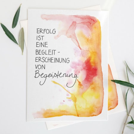 Eine Grußkarte mit Aquarellhintergrund in Gelb-, Orange- und Rottönen. In der Mitte steht der Text „Erfolg ist eine Randerscheinung von Begeisterung“ in Schreibschrift.