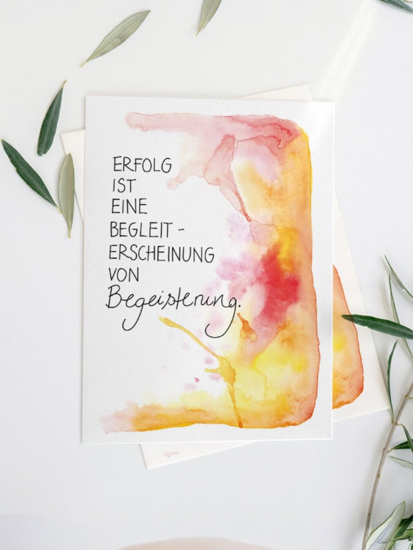 Eine Grußkarte mit Aquarellhintergrund in Gelb-, Orange- und Rottönen. In der Mitte steht der Text „Erfolg ist eine Randerscheinung von Begeisterung“ in Schreibschrift.