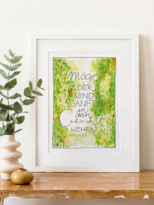 „Möge der Wind sanft in dein Gesicht wehen – Blessing #3“. Der Druck steht auf einem Holztisch neben einer weißen Vase mit Eukalyptuszweigen und einer kleinen Keramikschale. Helles, natürliches Licht, ruhige, warme Wohnatmosphäre.