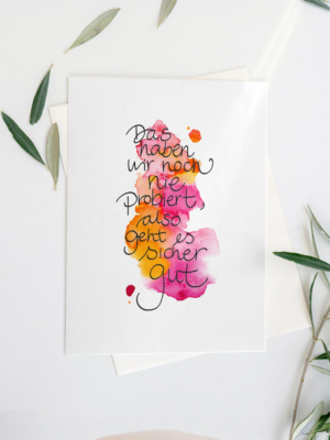 „Farbenfrohes Aquarell mit dem Zitat: ‚Das haben wir noch nie probiert, also geht es sicher gut‘ in verspielter Handschrift auf pink-orangem Farbverlauf.“