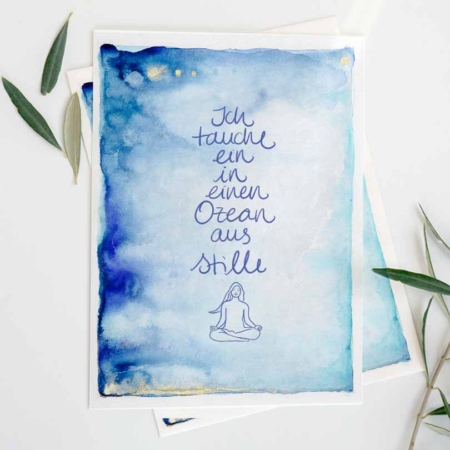 Eine Karte mit einem sanften Aquarell-Hintergrund in Blautönen, der an einen Himmel oder das Meer erinnert. In der Mitte steht in geschwungener blauer Schrift der Text 'Ich tauche ein in einen Ozean aus Stille.' Unter dem Text befindet sich eine minimalistische Zeichnung einer Person, die in einer Meditationshaltung sitzt. Oben links sind drei kleine goldene Punkte. Die Karte ist umgeben von grünen Olivenblättern.