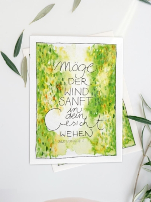 „Möge der Wind sanft in dein Gesicht wehen – Blessing #3“. Der Druck steht auf einem Holztisch neben einer weißen Vase mit Eukalyptuszweigen und einer kleinen Keramikschale. Helles, natürliches Licht, ruhige, warme Wohnatmosphäre.