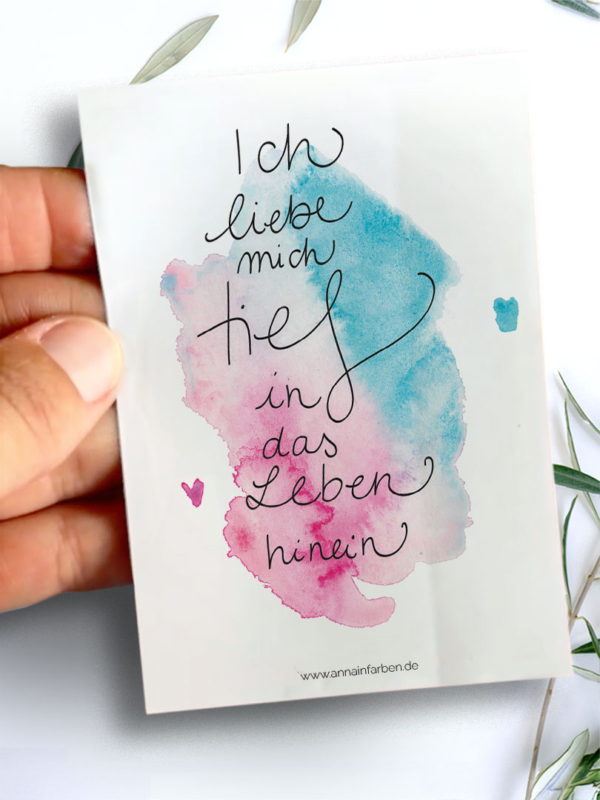 Sticker mit Aquarellhintergrund in Cyan- und Magentatönen. In der Mitte steht der Text „Ich liebe mich tief in mein Leben hinein“ in geschwungener Schreibschrift.