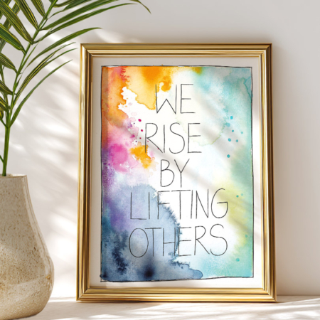 Ein Kunstdruck in Din A4 mit Aquarellhintergrund in Gelb-, Blau-, Grün- und Pinktönen. In der Mitte steht der Text „We rise by lifting others“ in Schreibschrift.