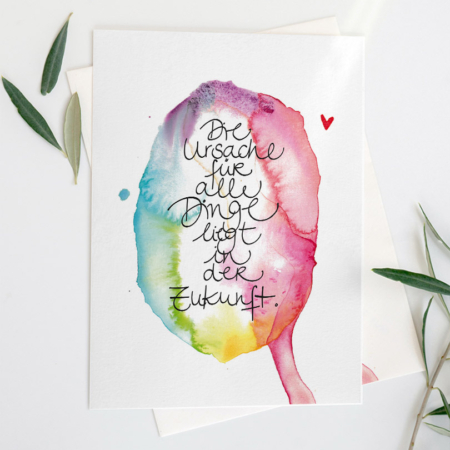 Postkarte eines Aquarells in lebendigen, ineinanderfließenden Farben – von kühlem Blau und Grün bis zu warmem Rot, Pink und Gelb. Im Zentrum steht in geschwungener, handgeschriebener Schrift der Satz: Die Ursache für alle Dinge liegt in der Zukunft.